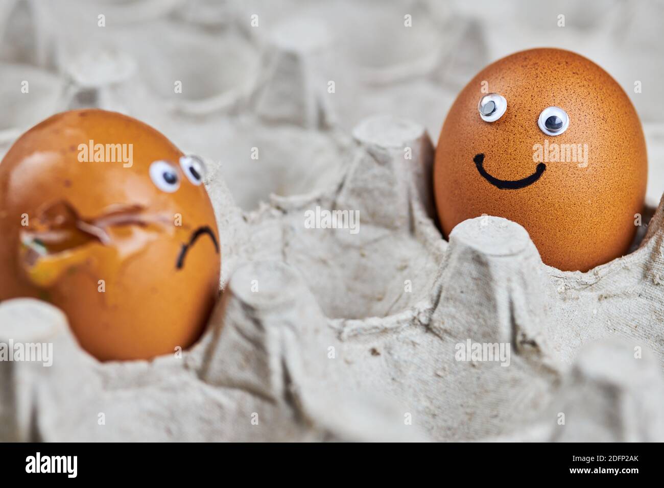 Funny egg and sad cracked egg in paper egg tray. Two easter 