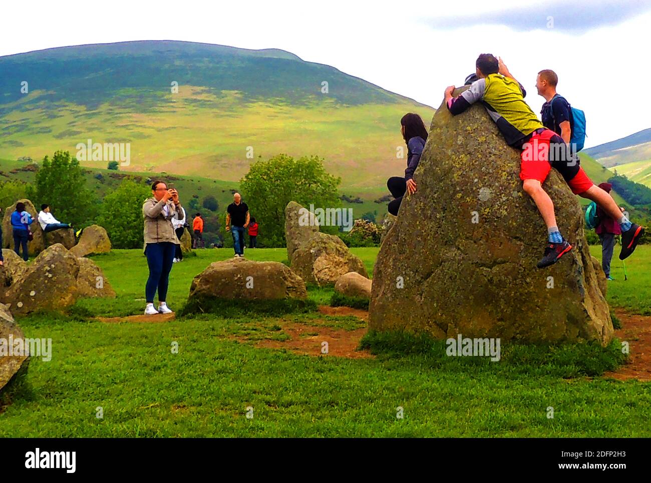 Over-enthusiastic tourists climb one of the largest stones for a photograph within the stunning  atmospheric  and dramatic setting of  Castlerigg ancient stone circle (Castle Lane, Underskiddaw, Keswick, Cumbria, CA12 4RN, UK). It has panoramic views all round  including the mountains of Helvellyn and High Seat as a backdrop. It was constructed circa  3000 / 400 BC during the Neolithic period. Stock Photo