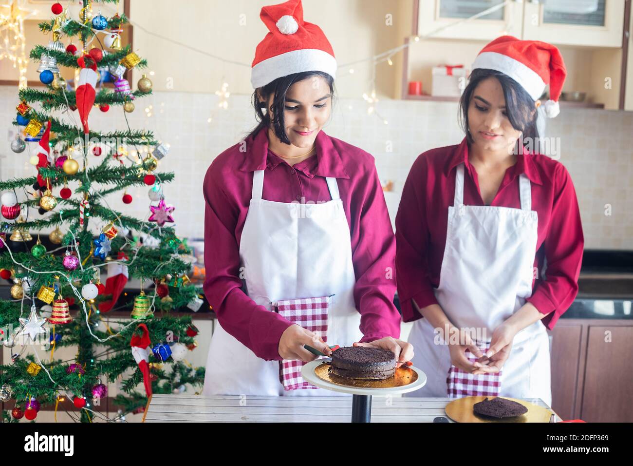 https://c8.alamy.com/comp/2DFP369/two-young-girls-wearing-chef-apron-and-santa-hat-preparing-christmas-cake-bread-at-home-with-decorated-tree-in-the-background-holiday-and-party-seaso-2DFP369.jpg