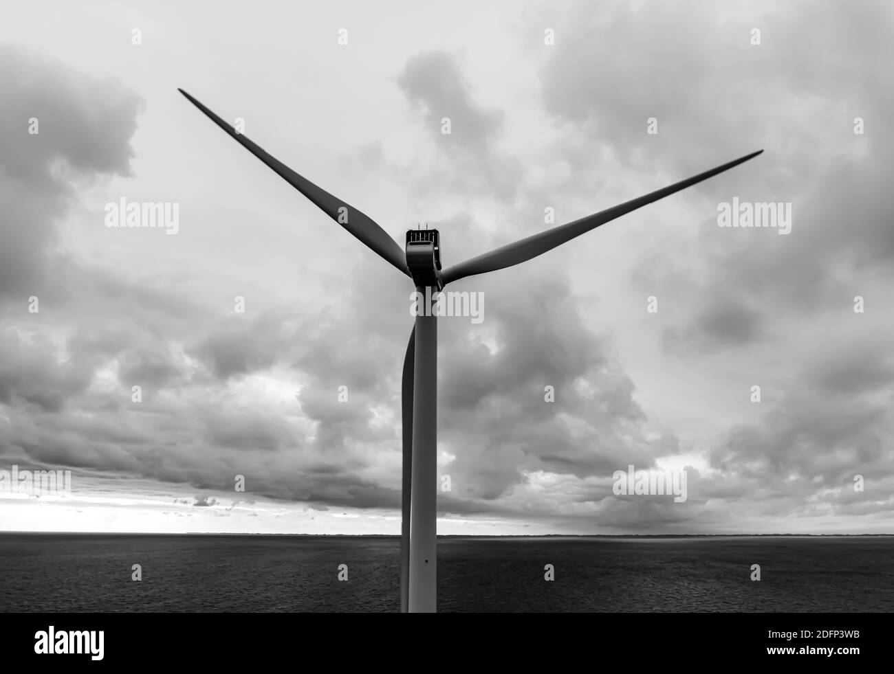 Black and white image of a modern wind turbine in the ocean with stormy clouds in the distance. Stock Photo