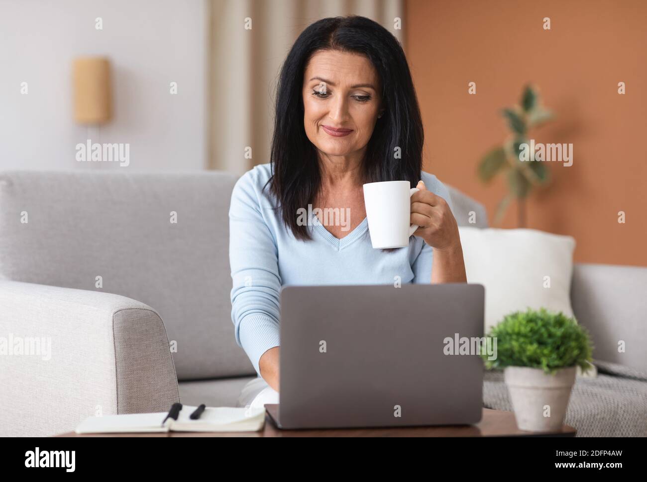 Mature woman holding coffe cup and working on computer Stock Photo