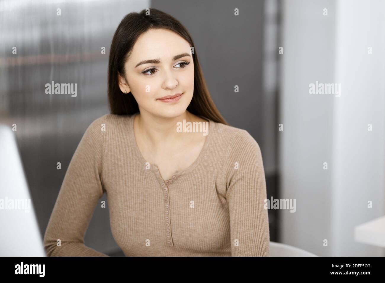 Portrait of beautiful business woman, while she is sitting at the desk ...