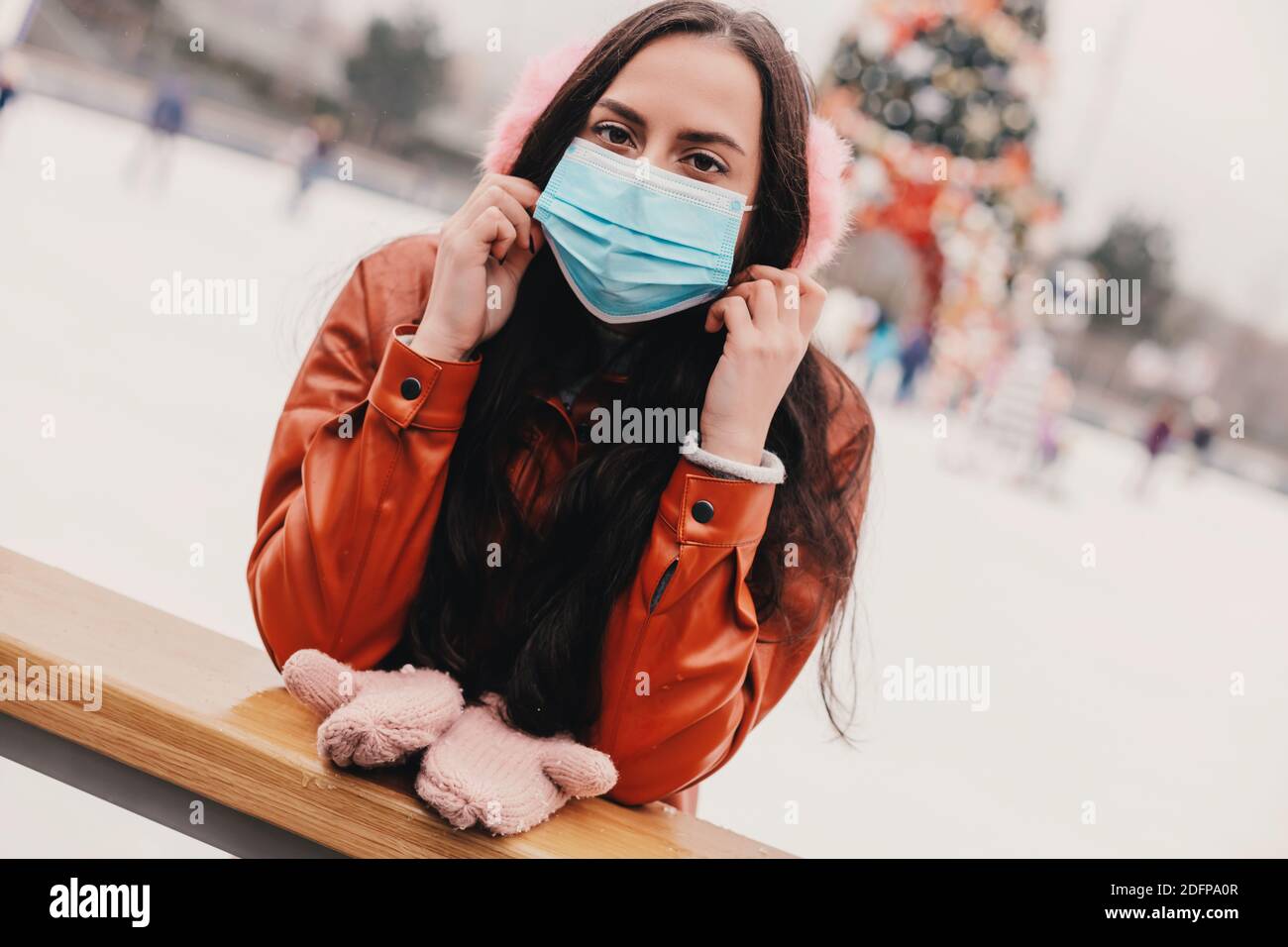 Stylish beautiful young woman in furry earmuffs put on medical face mask,  skate on outdoor ice rink. Happy attractive girl wear protective mask on  ice Stock Photo - Alamy