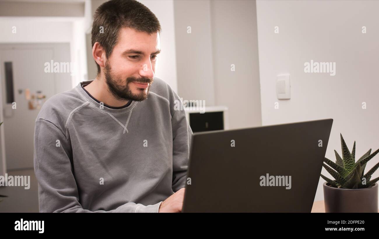 Man smiling and working at home on laptop computer. Stock Photo