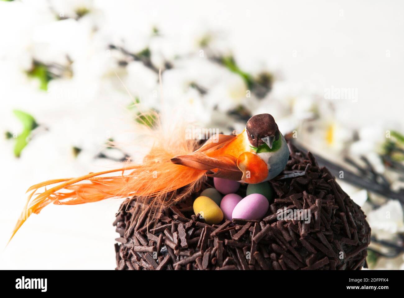 Easter chocolate cake and bird sitting in the nest. Little orange bird and colored eggs on a background of Easter’s décor Stock Photo