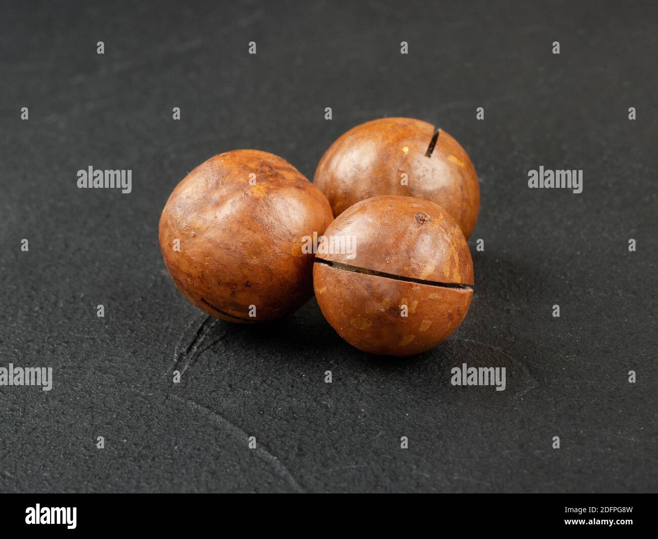 Three macadamia nuts on a dark concrete background Stock Photo