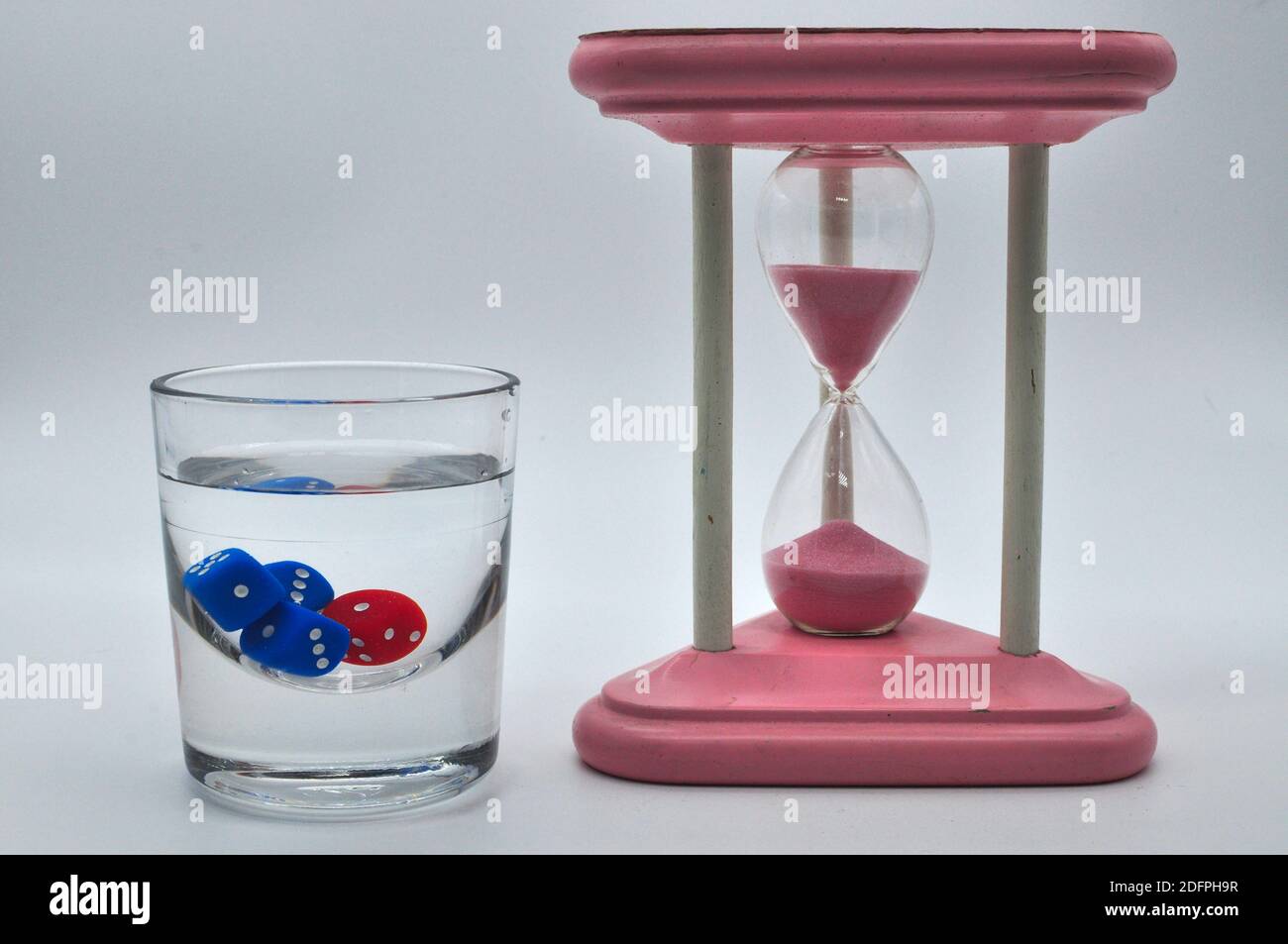 glass of alcohol containing red and blue dice with gorgeous vintage pink hourglass on white background Stock Photo