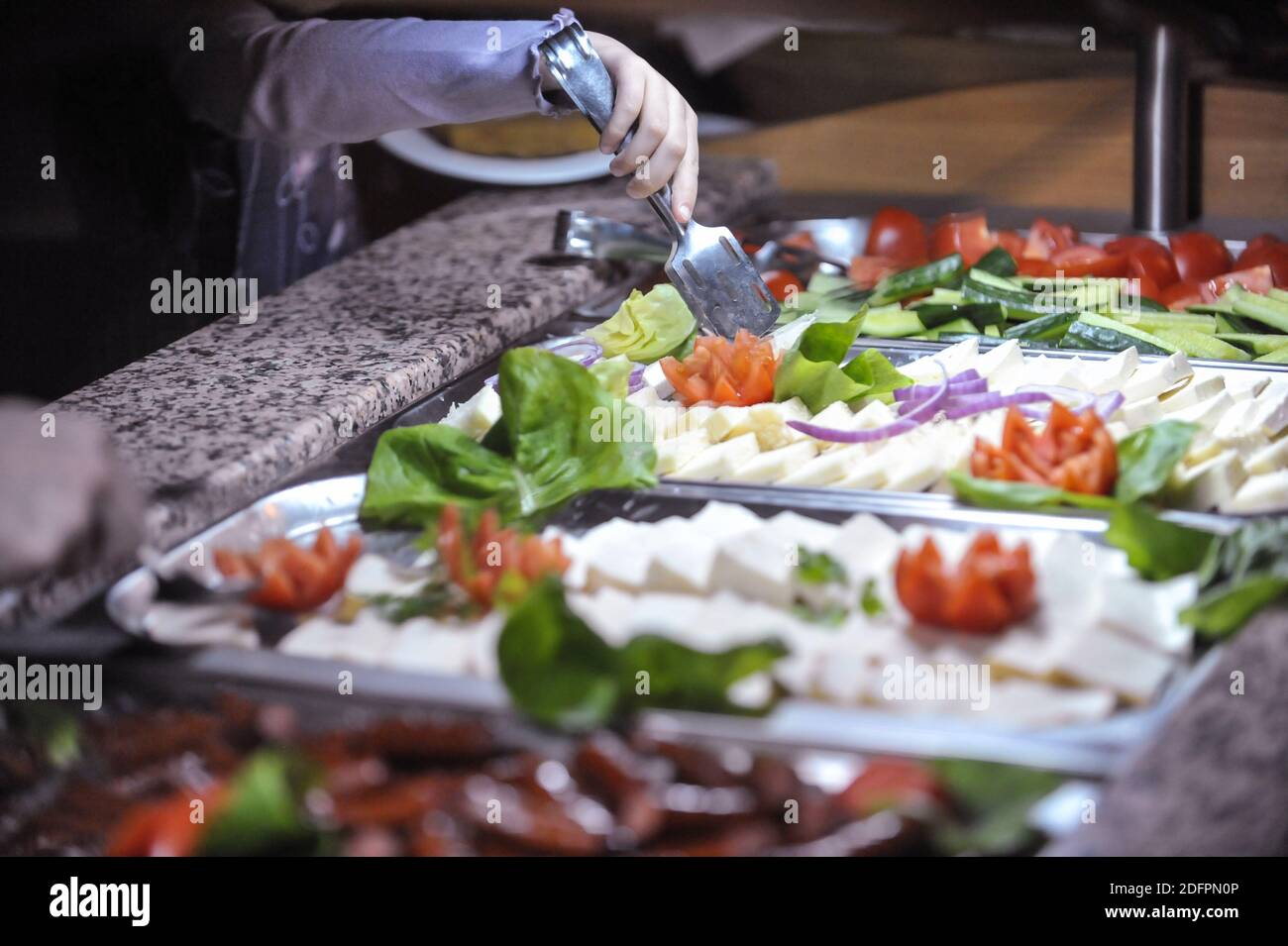Shallow depth of field (selective focus) image with the hand of a child picking vegetables and cheese from an open buffet. Stock Photo
