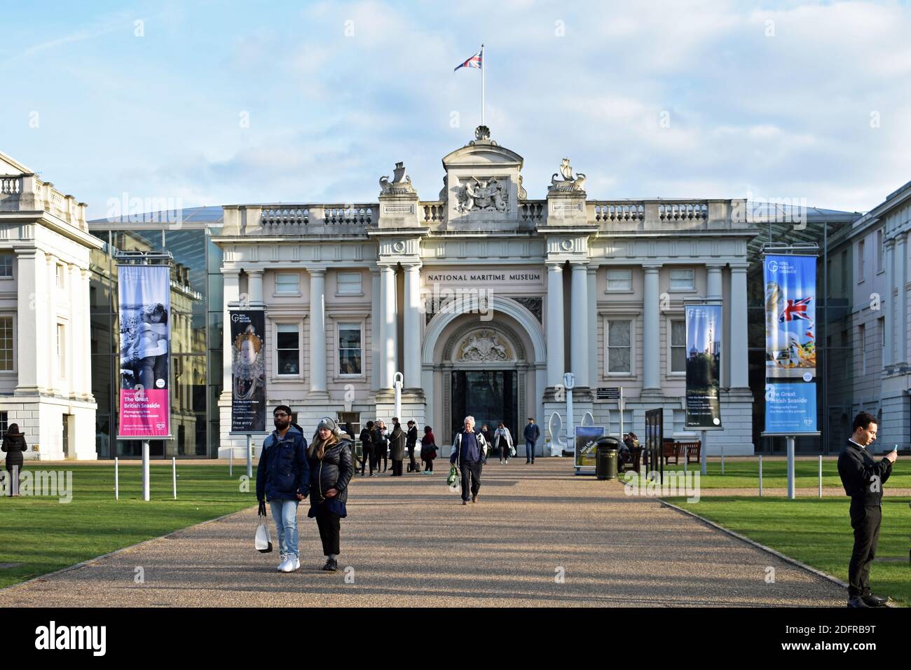 Visitors walk along the path that leads to the National Maritime Museum in Greenwich, London. Posters along the path advertise exhibitions. Stock Photo