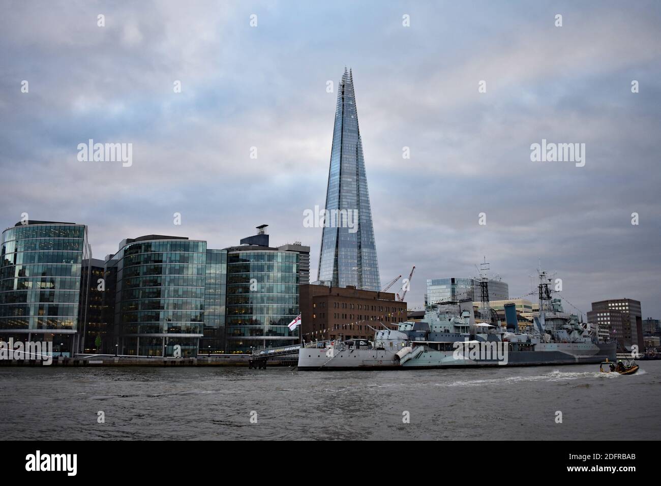 The Shard rises above buildings and the HMS Belfast warship museum from on the River Thames on an overcast day at dusk in London, UK Stock Photo