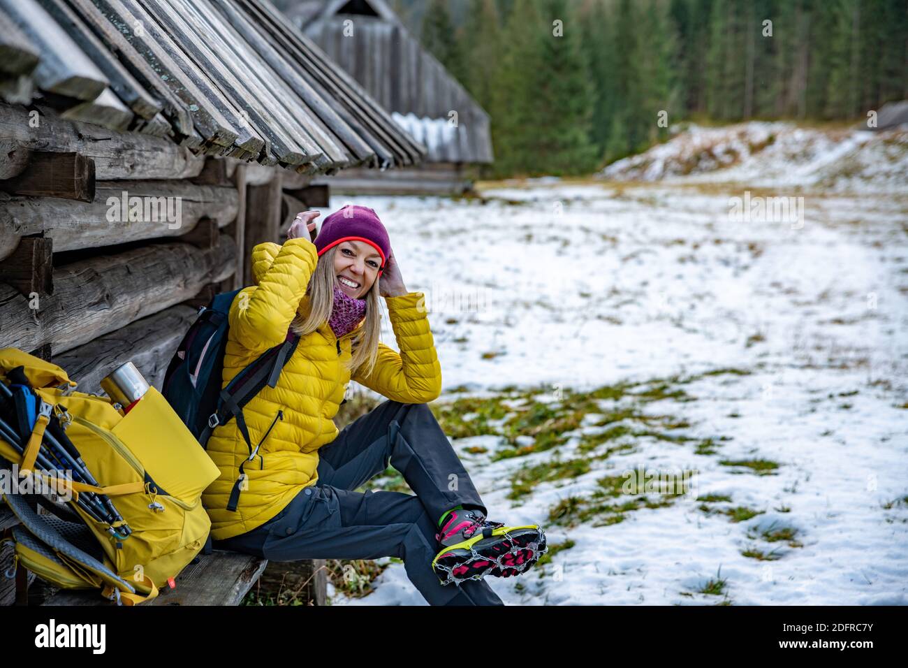 A smiling blonde tourist in a yellow down jacket is wearing crampons
