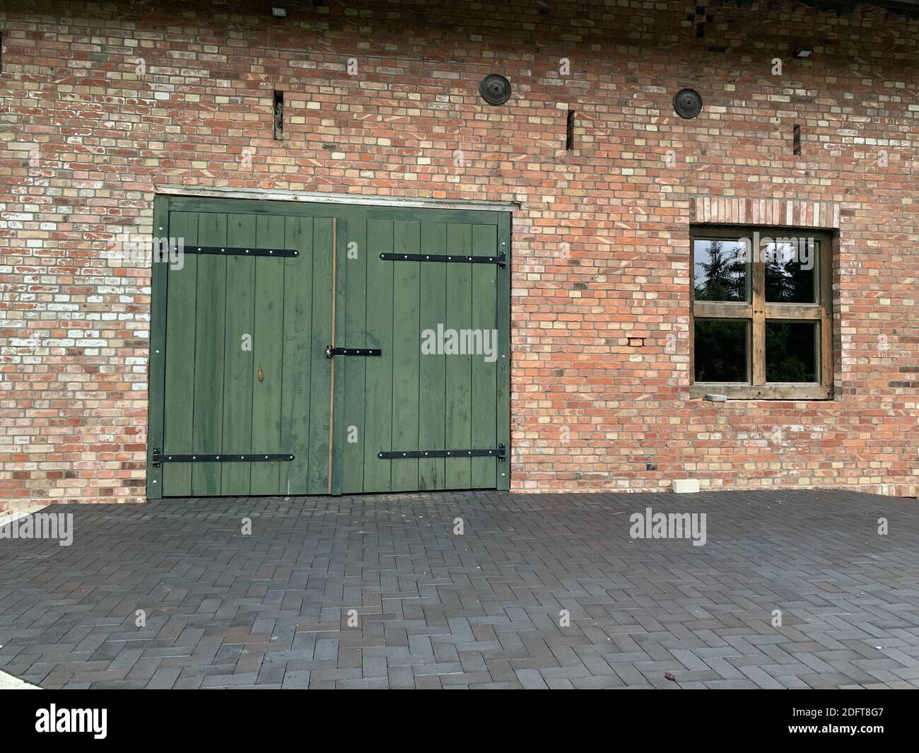 a green large door and a rectangular low window on a brick wall building Stock Photo
