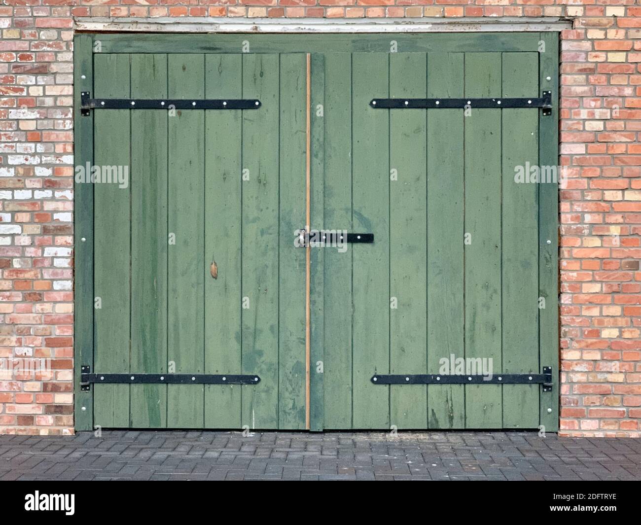 a green large door and a rectangular low window on a brick wall building Stock Photo