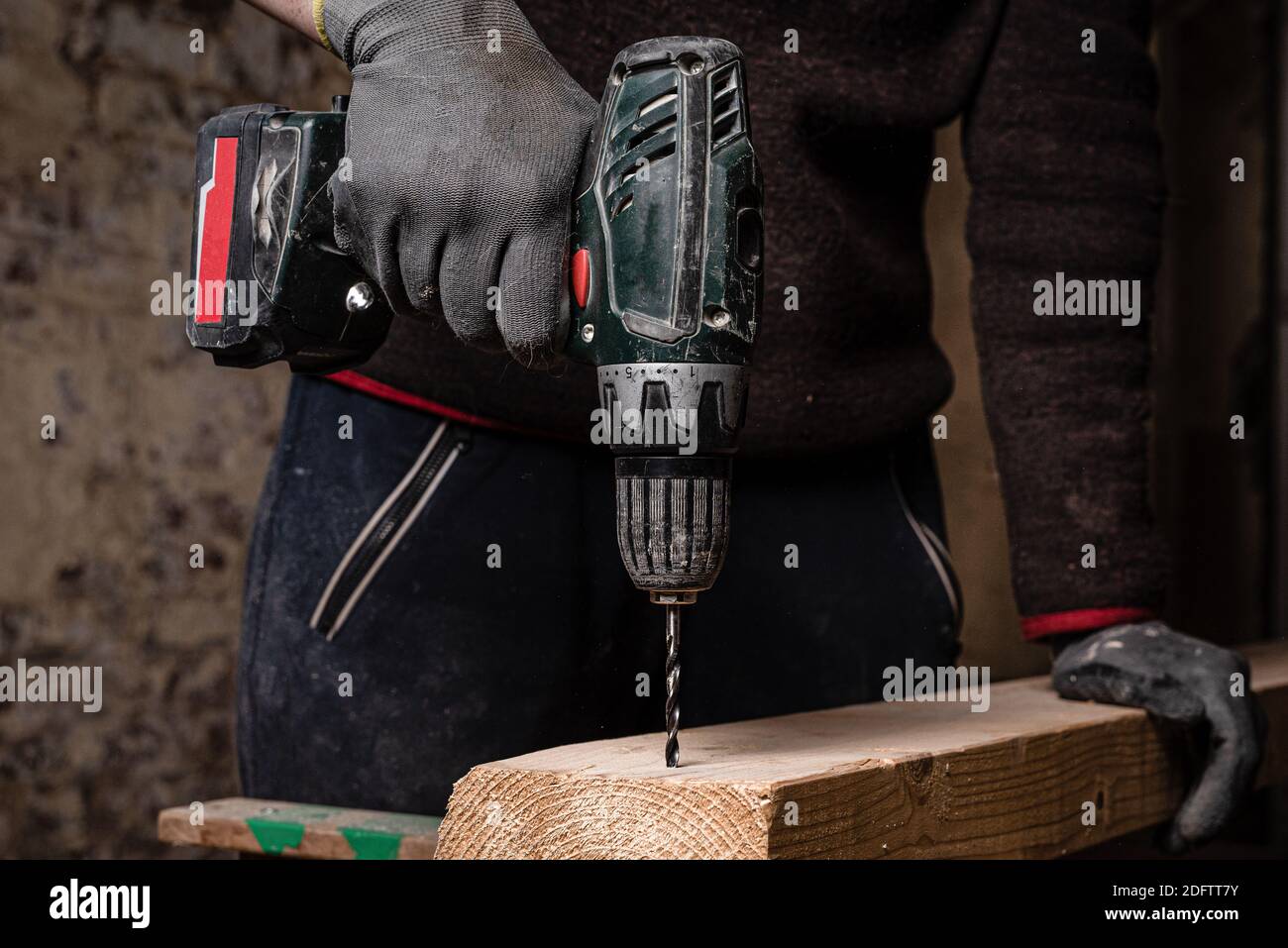 A closeup of a working man wearing safety work gloves and drilling a plank  of wood in the workshop Stock Photo - Alamy