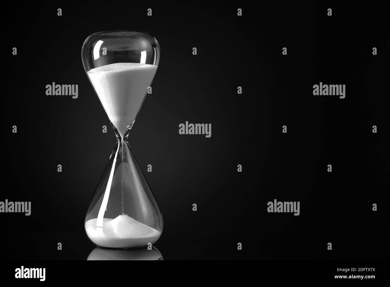 Hourglass with white sand on black background Stock Photo - Alamy