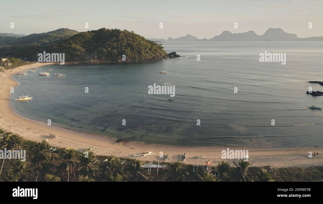 Traditional boats at sea bay aerial. Serene seascape at paradise island resort. Green forest on mountain. Sand beach at harbor. Summer cruise on passenger ships at open ocean. Cinematic rise up shot Stock Photo