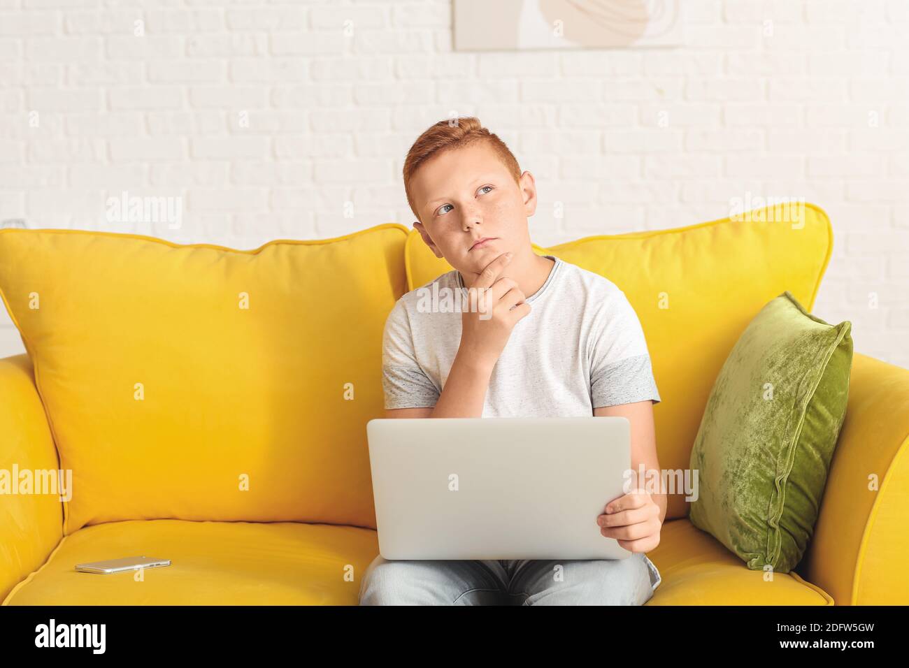Thoughtful teenage boy with laptop sitting on sofa at home Stock Photo ...