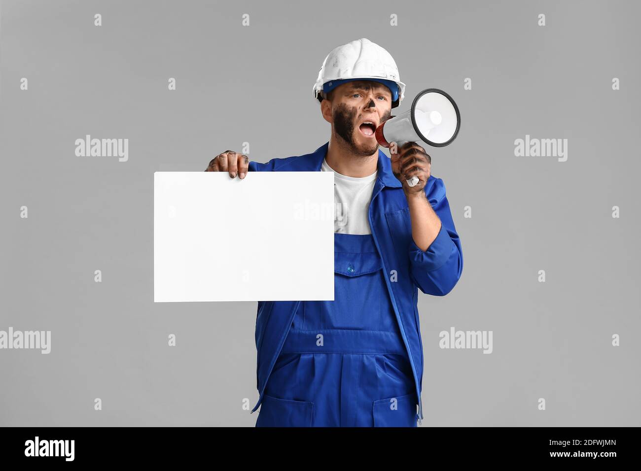 Protesting miner man with placard and megaphone on grey background Stock Photo