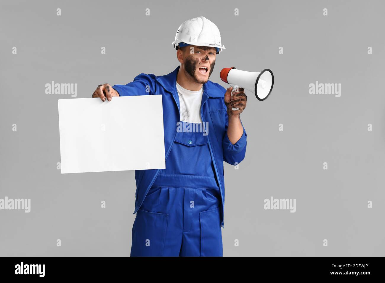Protesting miner man with placard and megaphone on grey background Stock Photo