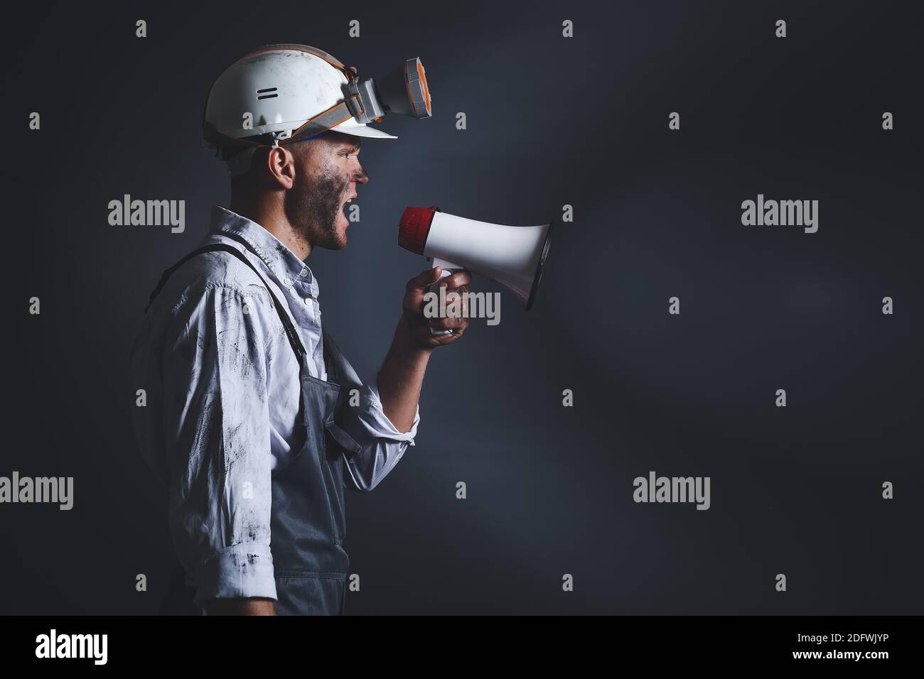 Protesting miner man with megaphone on dark background Stock Photo