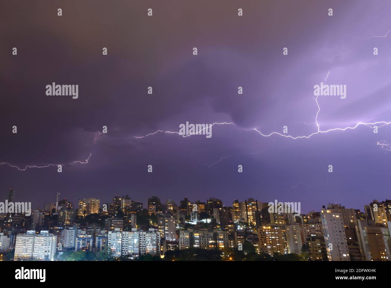 Skyline of Porto Alegre with stormy sky at night. Forked lightning spreading in the sky above residential buildings. Bad weather in South of Brazil. Stock Photo