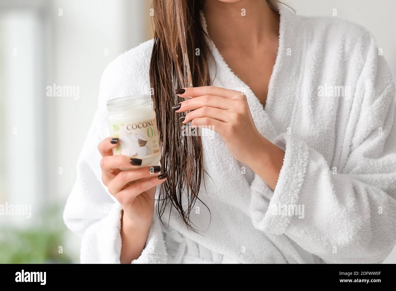 Beautiful young woman applying coconut oil on her hair in bathroom
