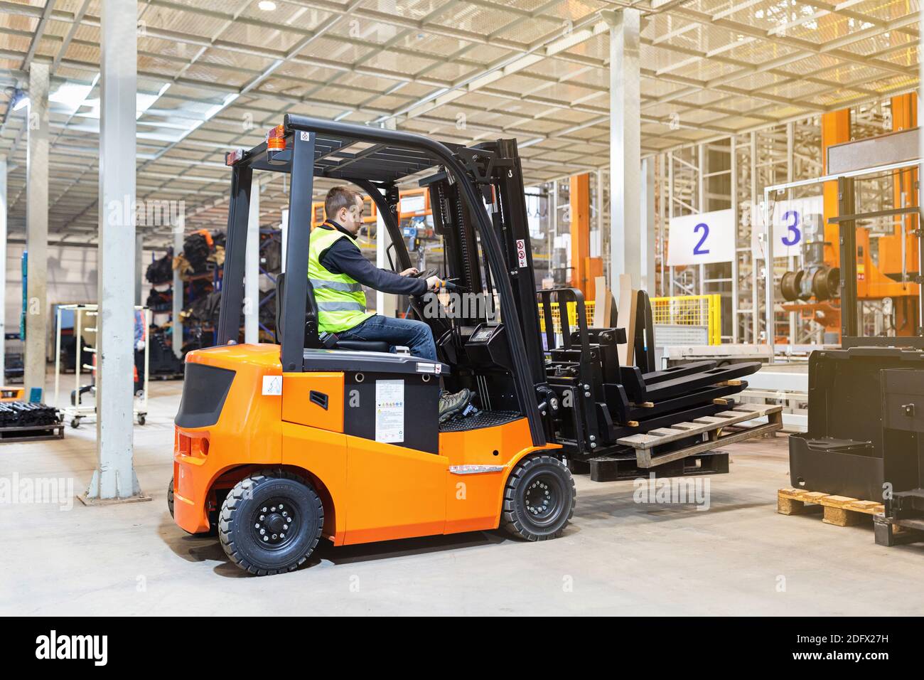 Storehouse employee in uniform working on forklift in modern automatic warehouse. Boxes are on the shelves of the warehouse. Warehousing, machinery Stock Photo