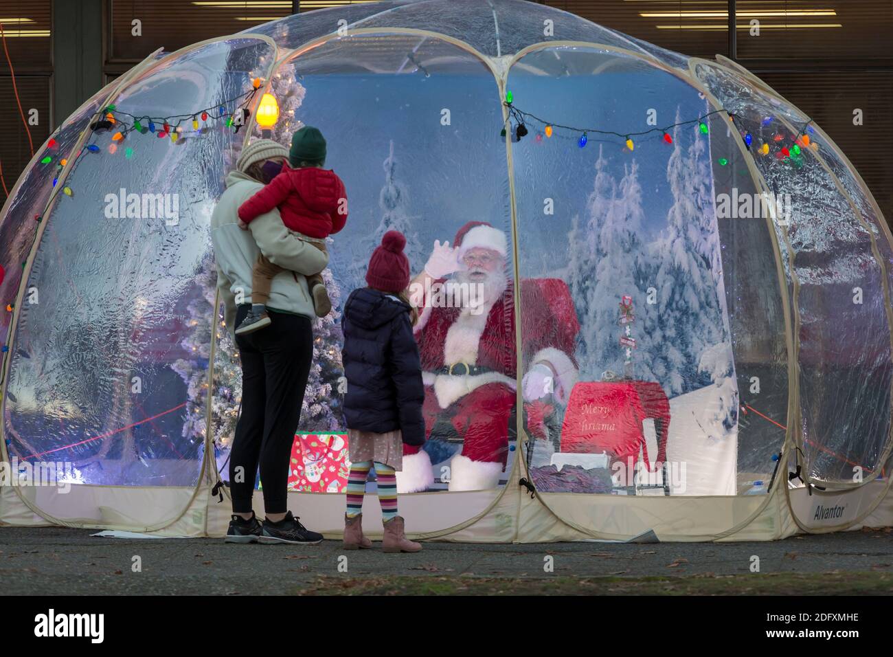 Seattle, Washington, USA. 6th December, 2020. Dan Kemmis, known as the Seattle Santa, greets a young family from within a protective plastic bubble in Seattle’s Greenwood neighborhood. Unable to schedule private events due to the coronavirus pandemic, Kemmis is making physically distanced public appearances with some donations benefiting local homeless shelters. Credit: Paul Christian Gordon/Alamy Live News Stock Photo