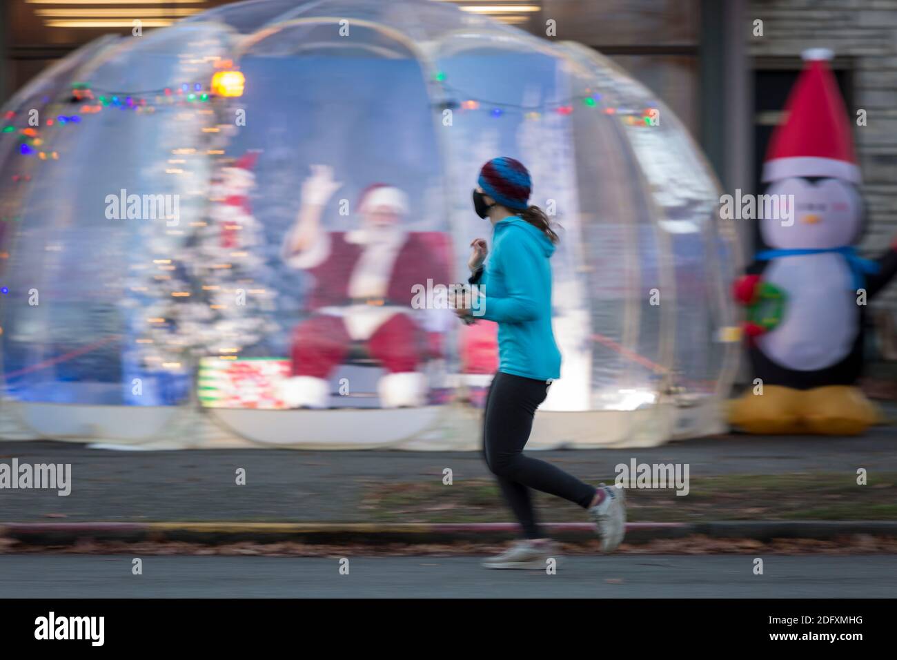 Seattle, Washington, USA. 6th December, 2020. Dan Kemmis, known as the Seattle Santa, waves to a runner from within a protective plastic bubble in Seattle’s Greenwood neighborhood. Unable to schedule private events due to the coronavirus pandemic, Kemmis is making physically distanced public appearances with some donations benefiting local homeless shelters. Credit: Paul Christian Gordon/Alamy Live News Stock Photo