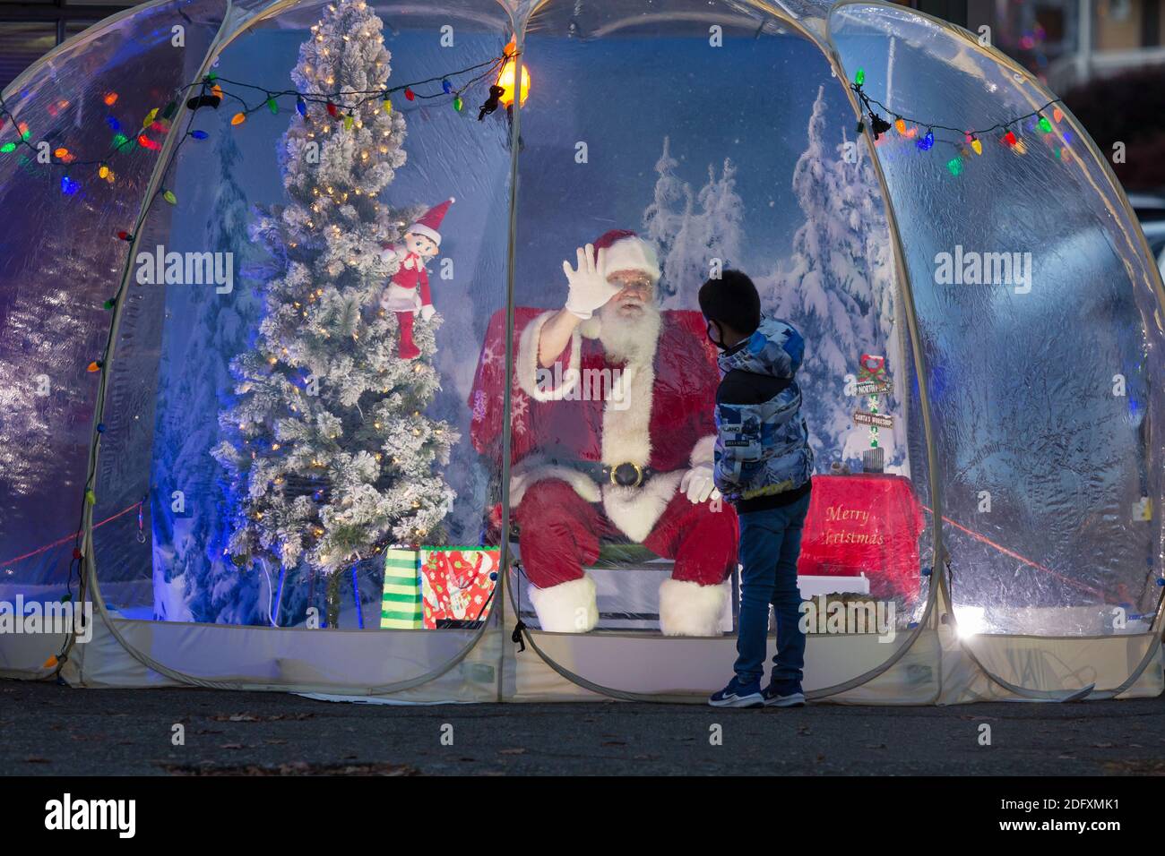 Seattle, Washington, USA. 6th December, 2020. Dan Kemmis, known as the Seattle Santa, high fives a young boy from within a protective plastic bubble in Seattle’s Greenwood neighborhood. Unable to schedule private events due to the coronavirus pandemic, Kemmis is making physically distanced public appearances with some donations benefiting local homeless shelters. Credit: Paul Christian Gordon/Alamy Live News Stock Photo