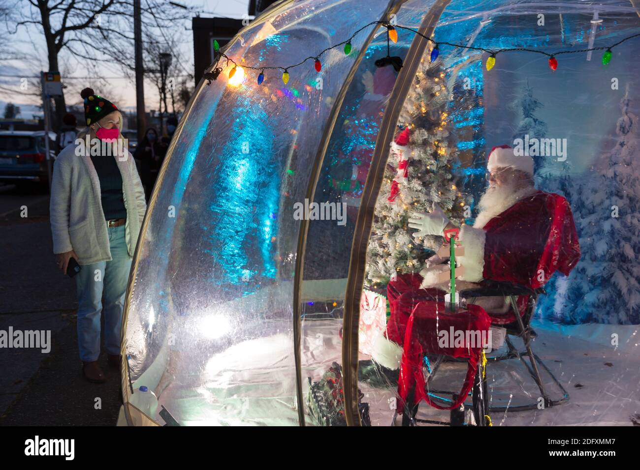 Seattle, Washington, USA. 6th December, 2020. Dan Kemmis, known as the Seattle Santa, chats with Kris Bennett from within a protective plastic bubble in Seattle’s Greenwood neighborhood. Unable to schedule private events due to the coronavirus pandemic, Kemmis is making physically distanced public appearances with some donations benefiting local homeless shelters. Credit: Paul Christian Gordon/Alamy Live News Stock Photo