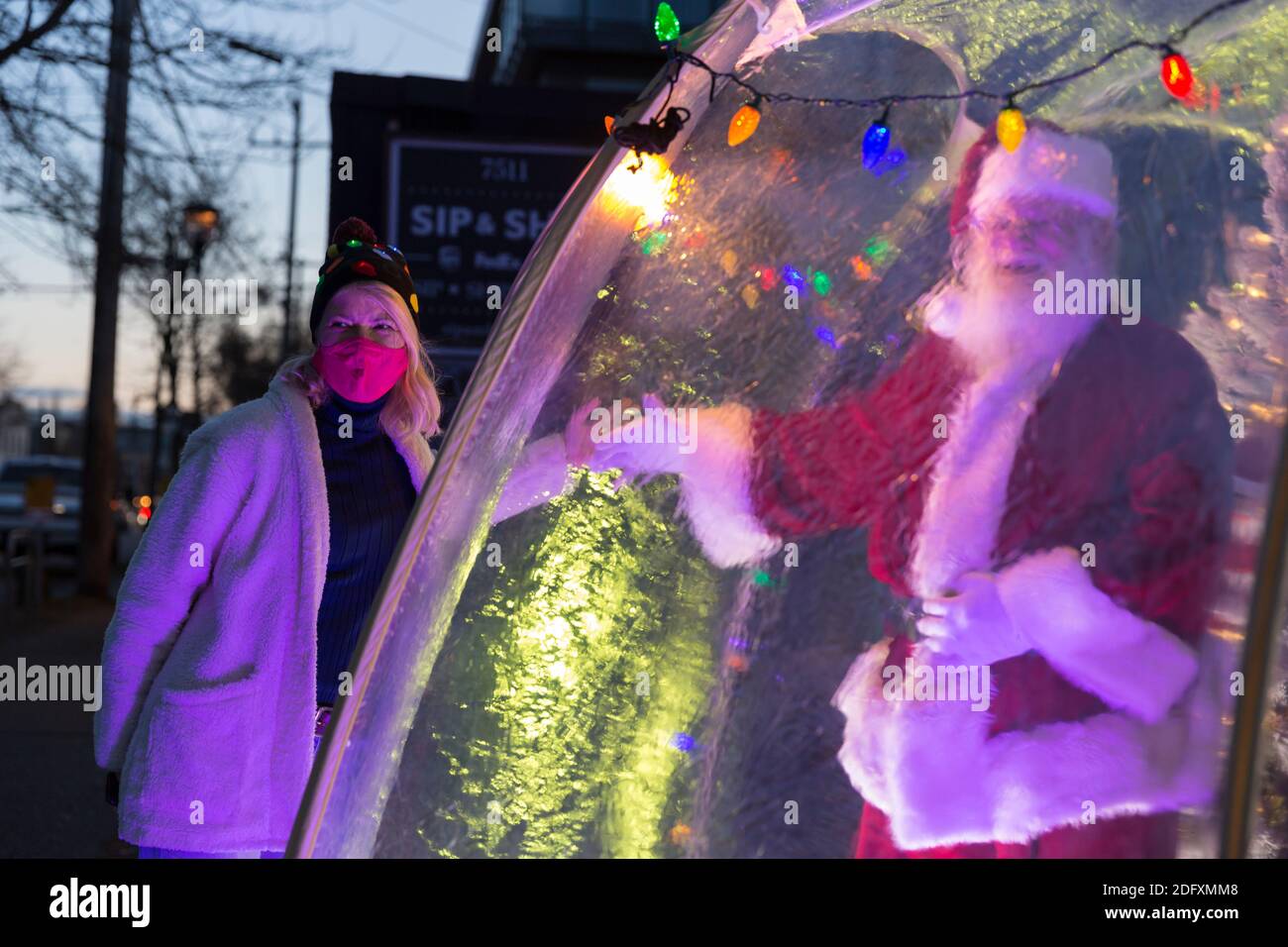 Seattle, Washington, USA. 6th December, 2020. Dan Kemmis, known as the Seattle Santa, poses for a photo with Kris Bennett from within a protective plastic bubble in Seattle’s Greenwood neighborhood. Unable to schedule private events due to the coronavirus pandemic, Kemmis is making physically distanced public appearances with some donations benefiting local homeless shelters. Credit: Paul Christian Gordon/Alamy Live News Stock Photo