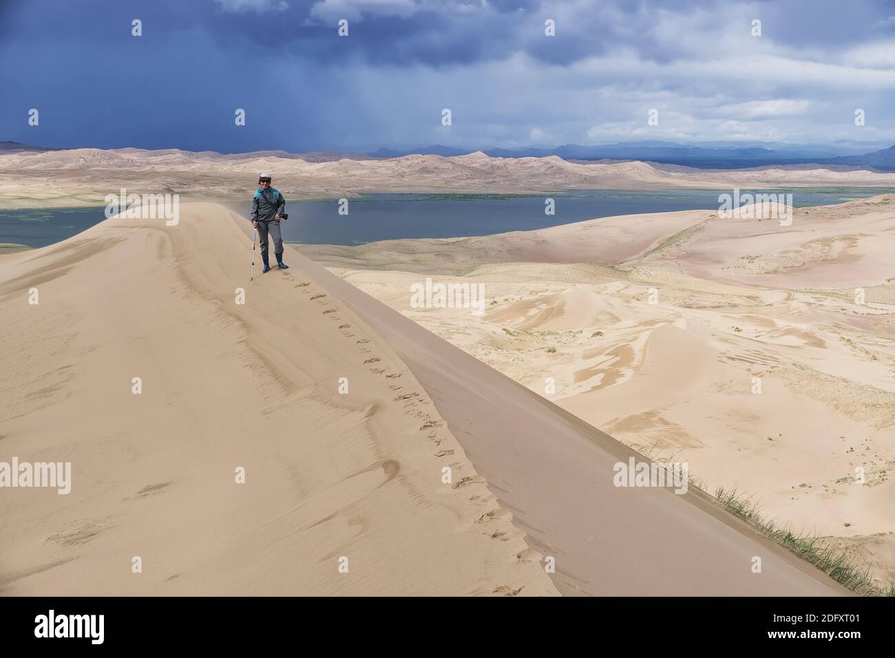 Tourist walking along the edge of the sand dune. Large barkhan in Mongolia sandy dune desert Mongol Els. Govi-Altay, Mongolia. Stock Photo