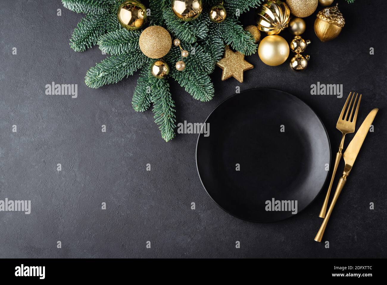 Christmas or New Year table setting background with black plate and golden color cutlery. Top view with copy space for text, design elements, graphics Stock Photo