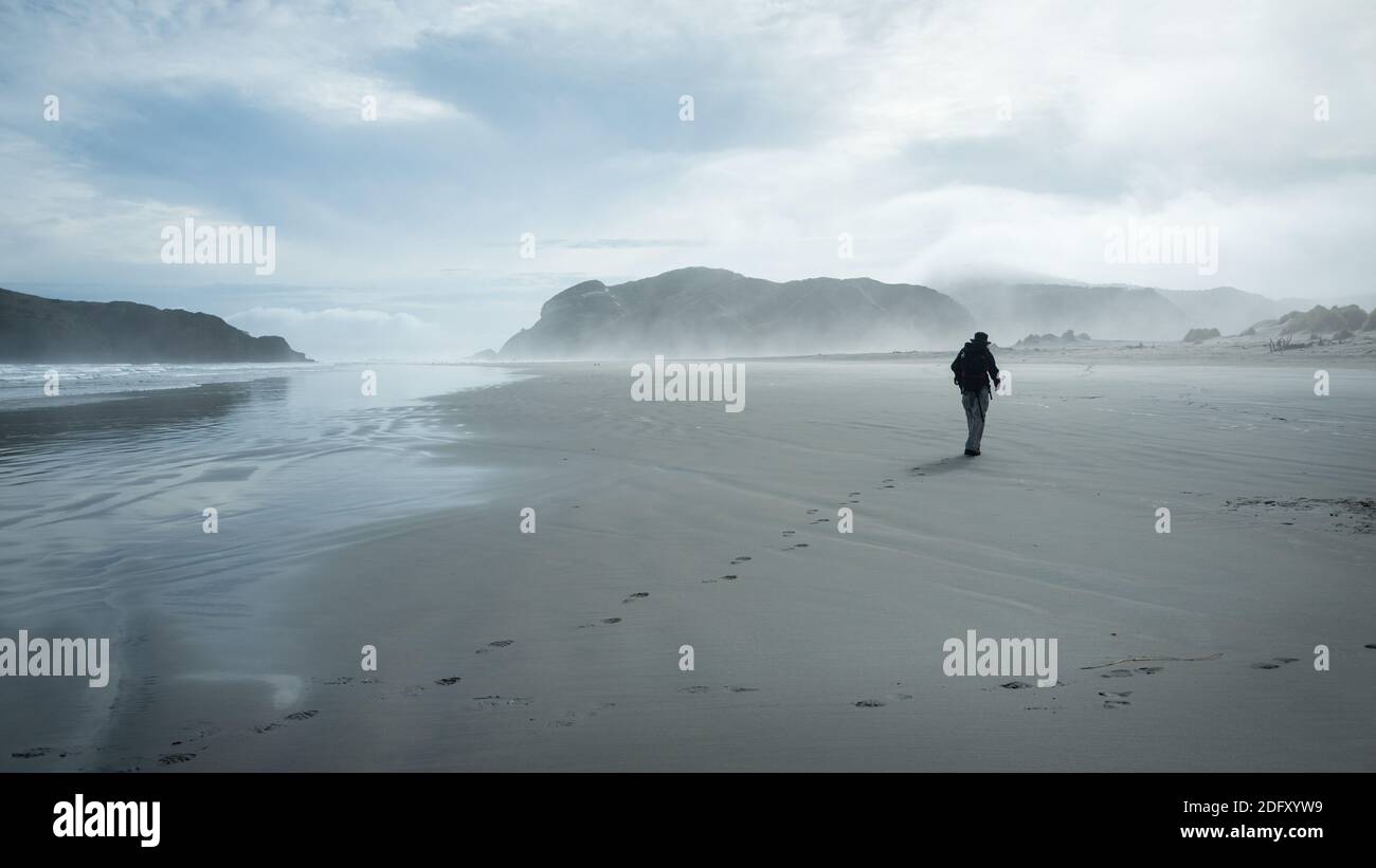 A backpacker walking on the sandy beach leaving the footprints, Wharariki Beach, South Island, New Zealand Stock Photo