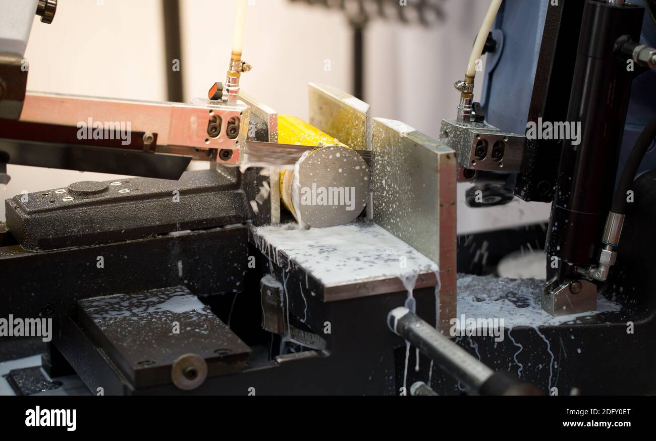 Band saw machine cutting metal rod and cooling with coolant. Industrial
