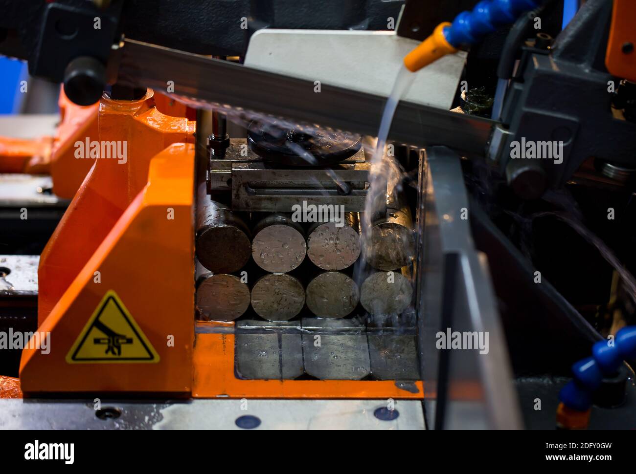 Band saw machine cutting metal rod and cooling with coolant. Industrial metalworking machinery