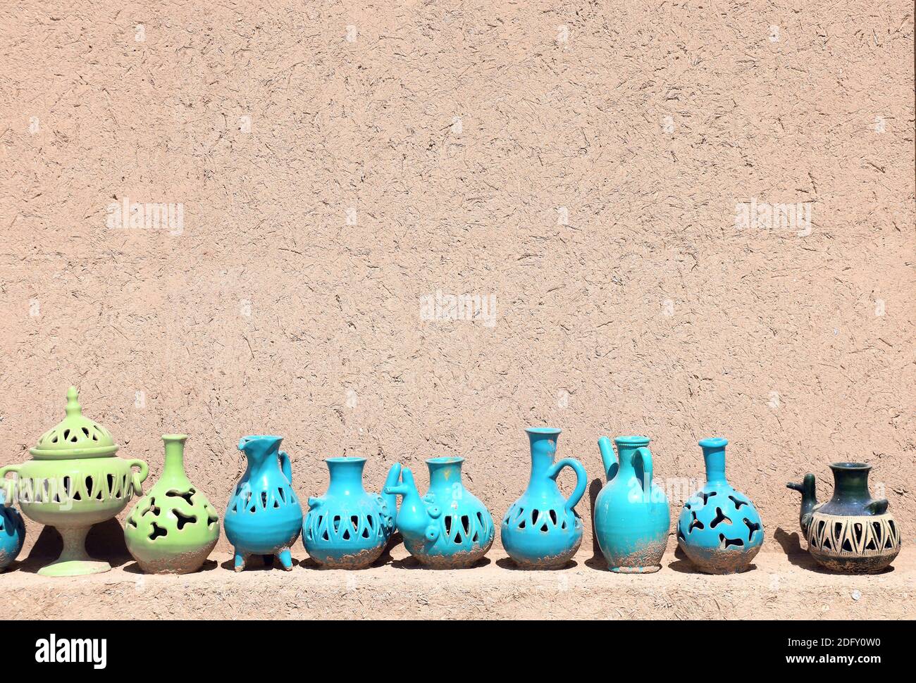Traditional iranian souvenirs - colorful clay pot and jug, Yazd, Iran. Clay jugs of various shapes of green and blue colors on a shelf near the adobe Stock Photo