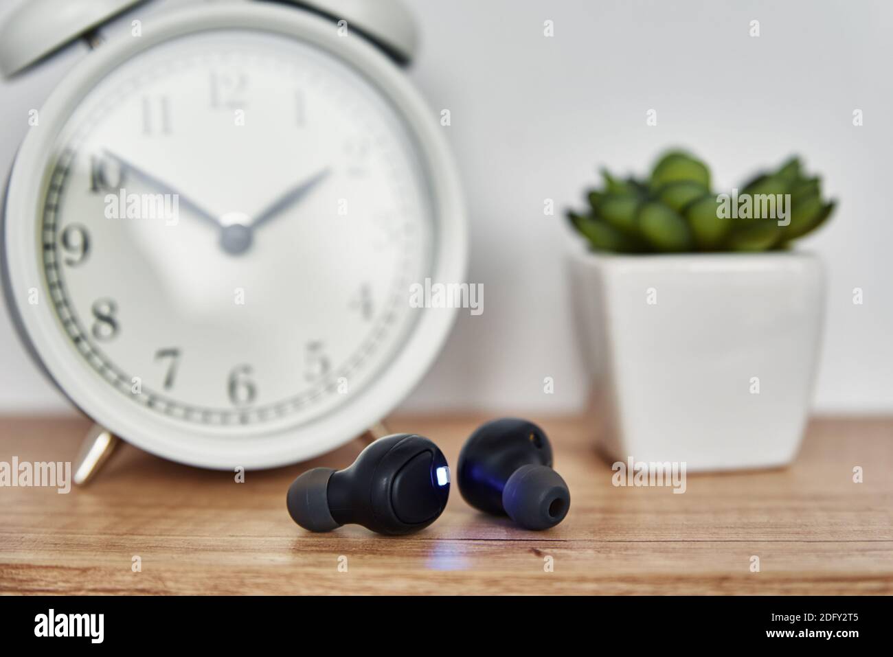 Wireless earphones on the shelf with alarm clock and house plant