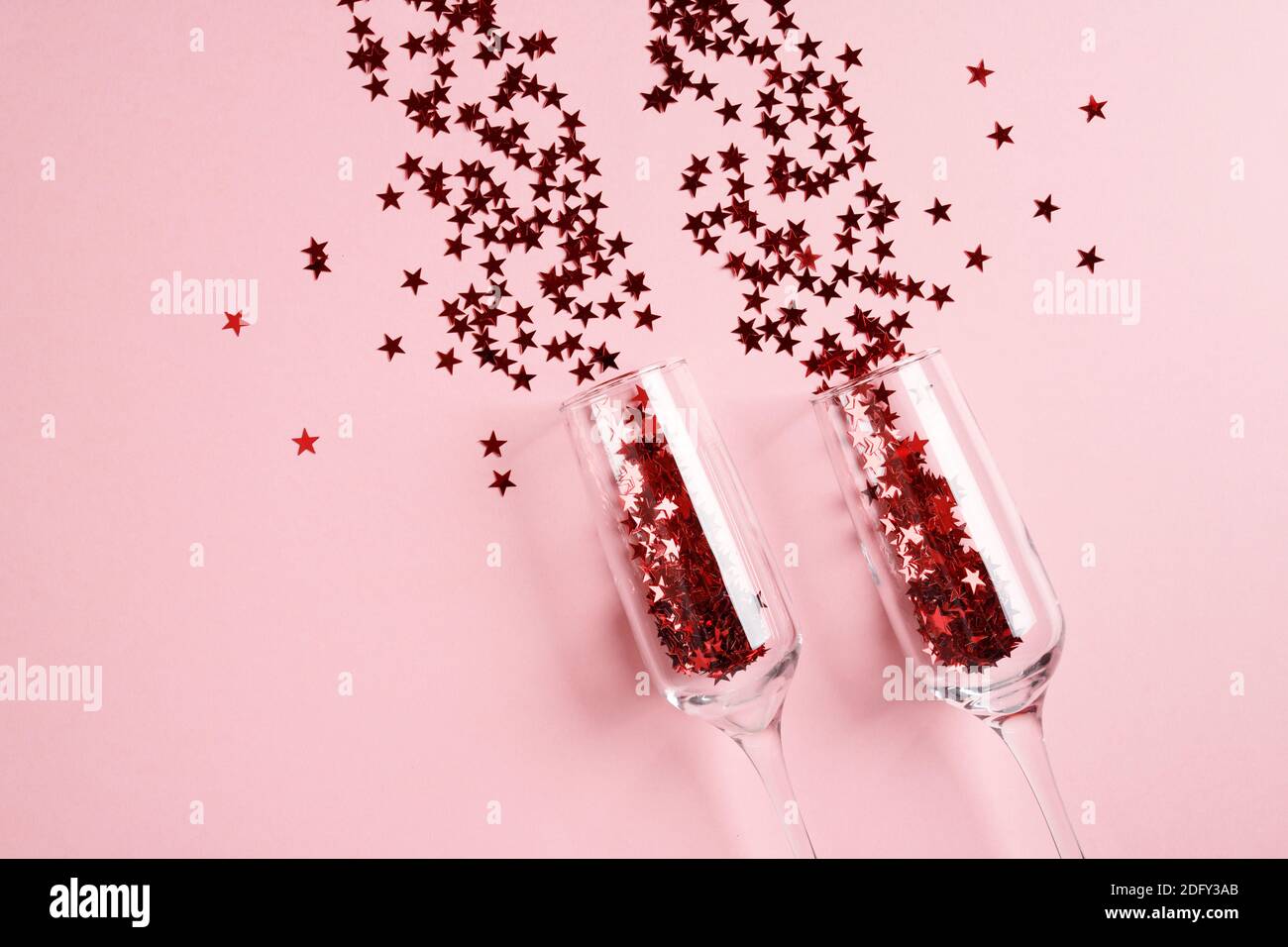 Champagne glasses with red confetti on pink background. Flat lay, top view celebrate party concept. Stock Photo
