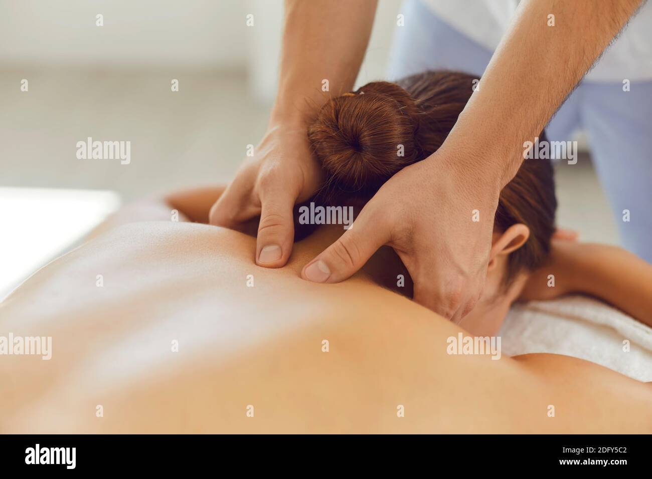 Young woman enjoying relaxing remedial body massage done by professional masseur Stock Photo