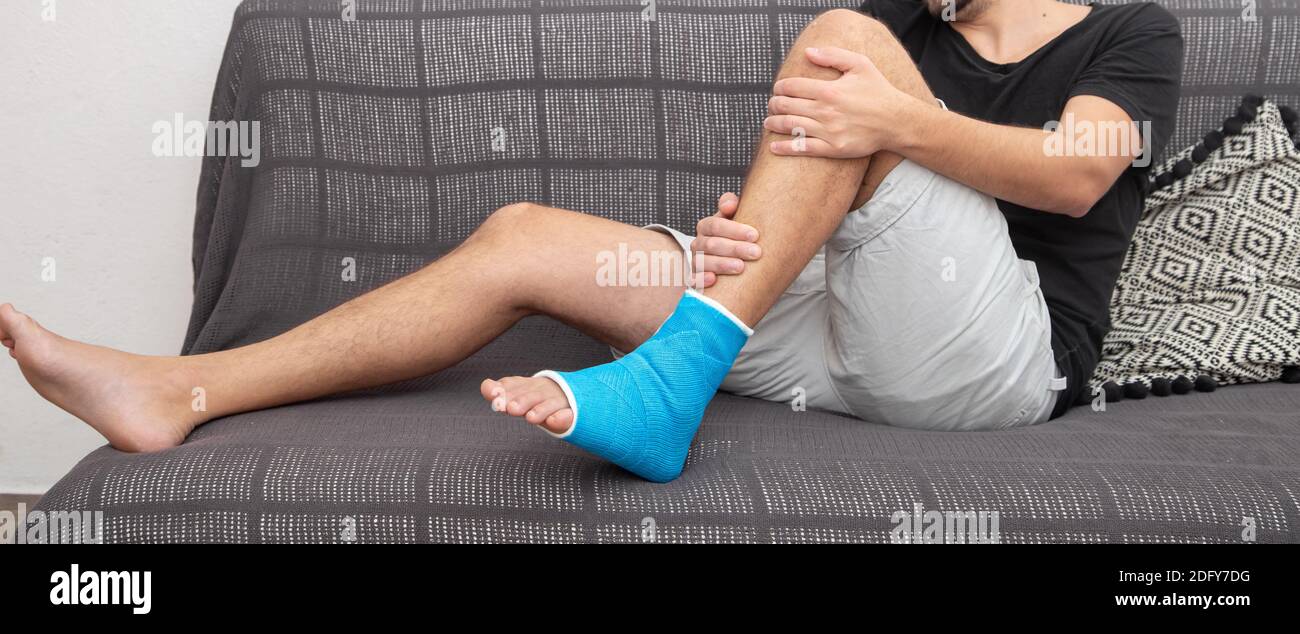 Bone fracture foot and leg on male patient and orthopaedic recovery lying on sofa staying at blue splint ankle. Stock Photo