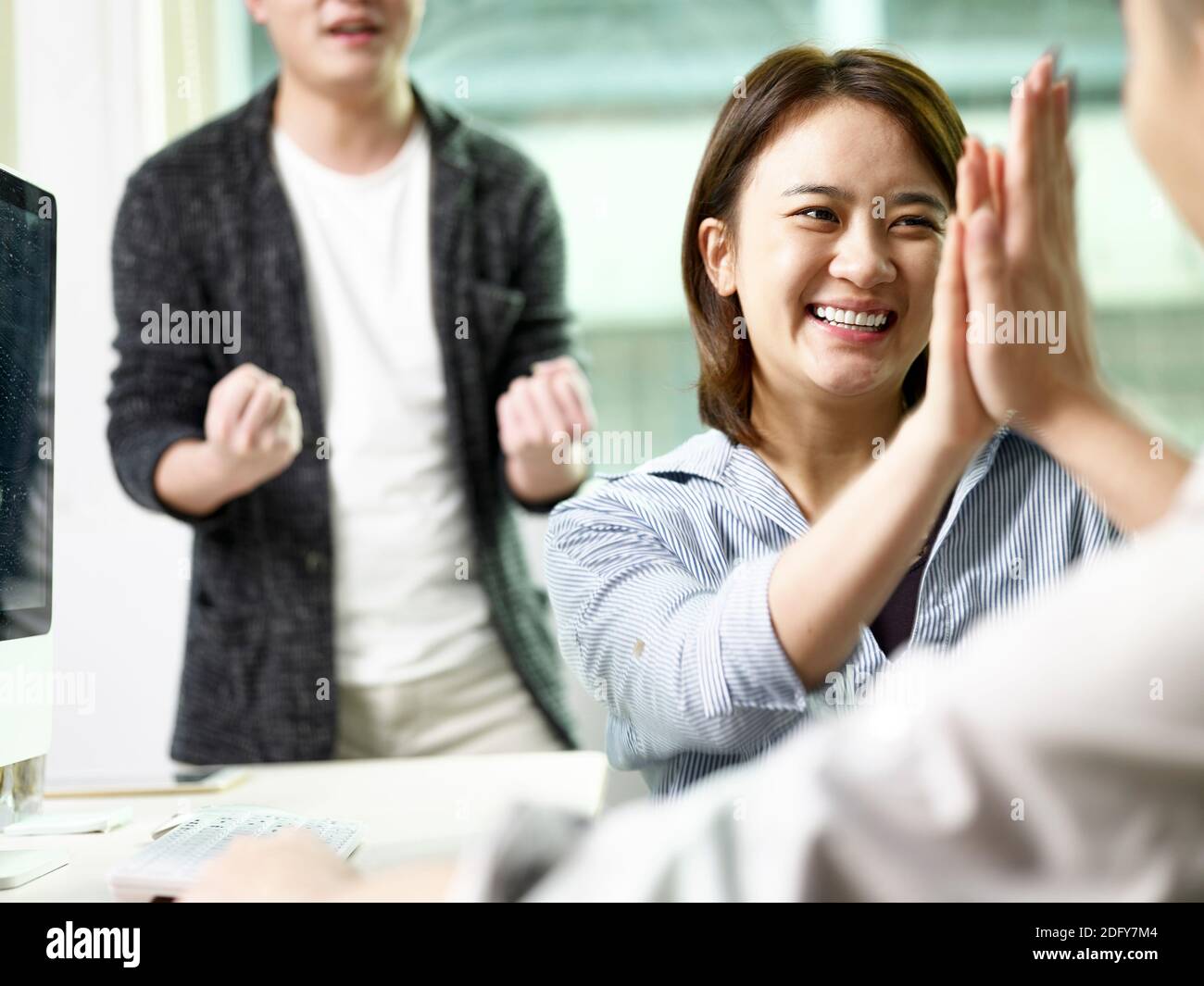 team of three asian business people giving hi-five celebrating achievement and success in office Stock Photo