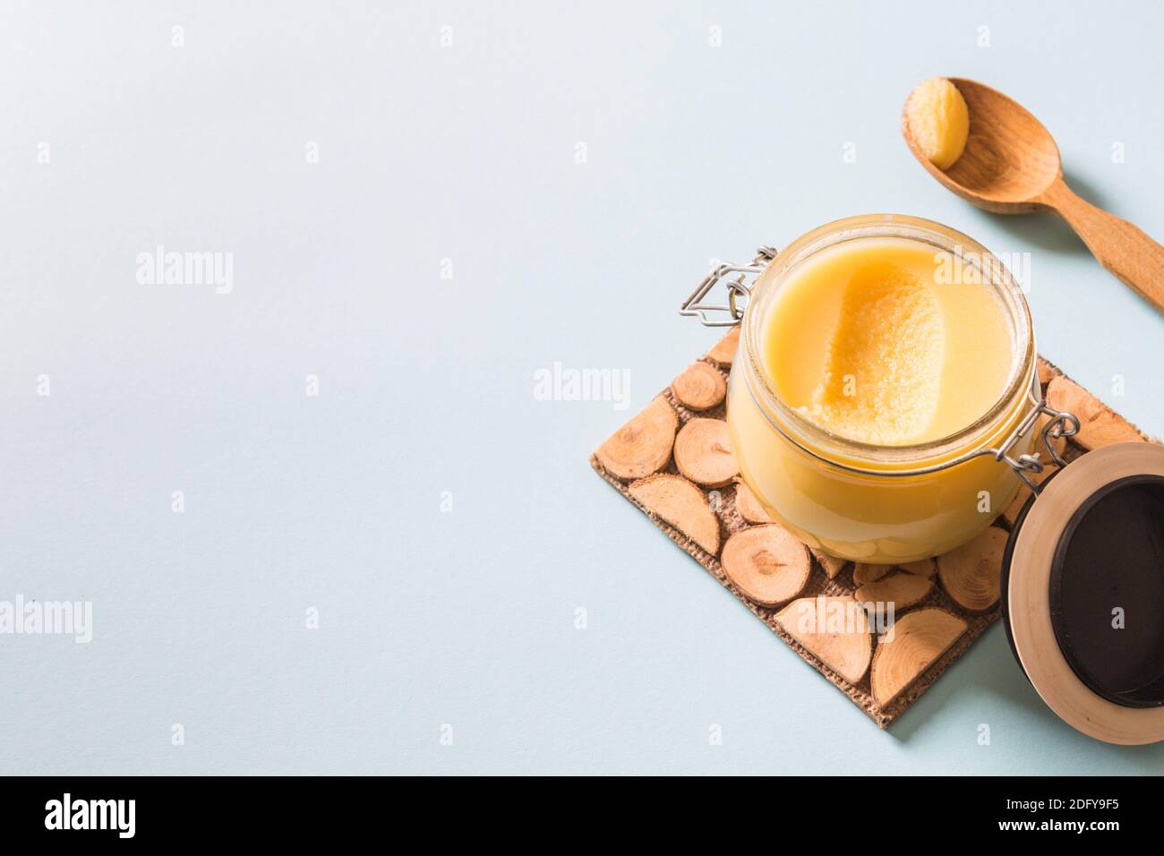 Ghee or clarified butter in jar and wooden spoon on blue background