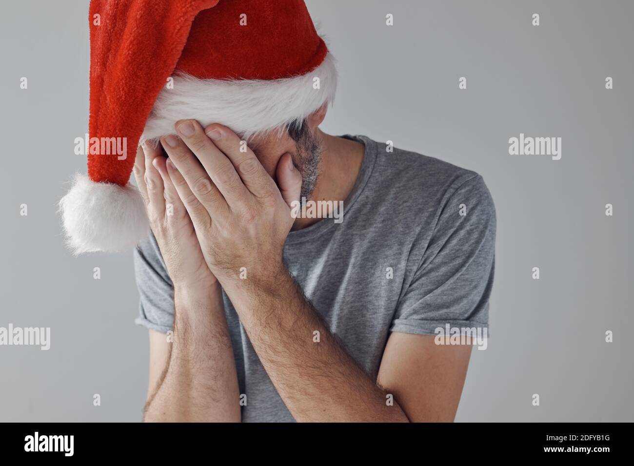 Christmas holiday depression, sad sulking man with Santa Claus hat covering face with his hands and crying alone in time of sadness, self-reflection, Stock Photo
