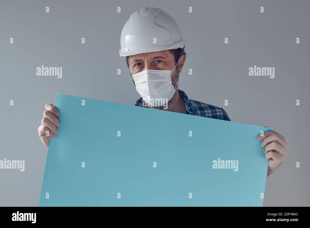 Construction engineer with white safety helmet and protective mask holding blank paper poster as copy space for text of graphics Stock Photo