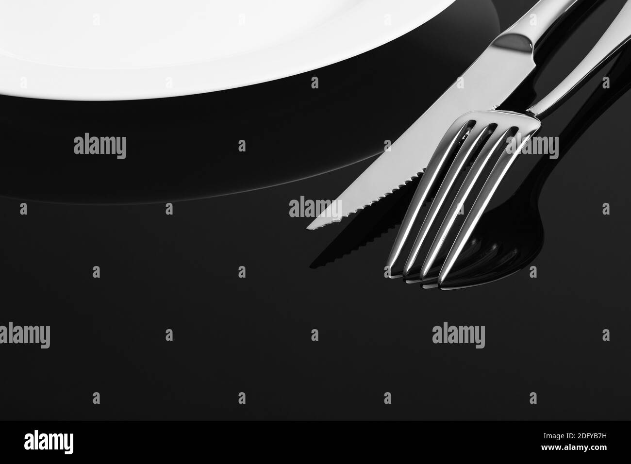 Close-up of fork, knife and empty plate on the black backround with space for text. Stock Photo