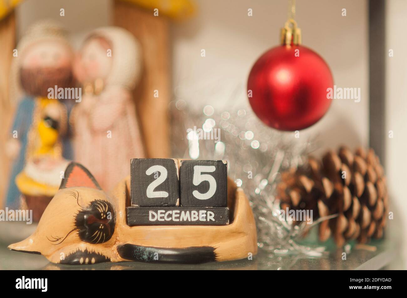 Cat-shaped wooden calendar surrounded by the nativity and other Christmas decorations shows the date of December 25th Stock Photo
