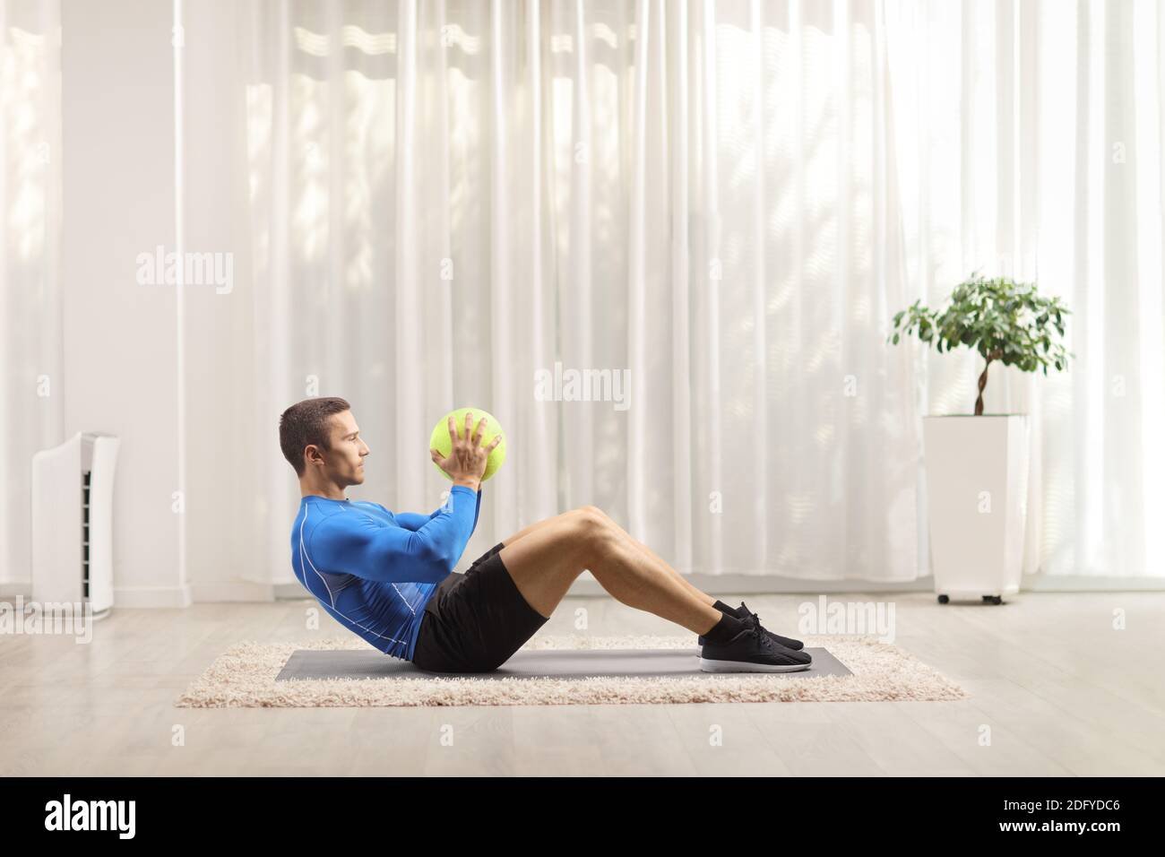 Young man in sportswear exercising with a ball on the floor at home Stock Photo