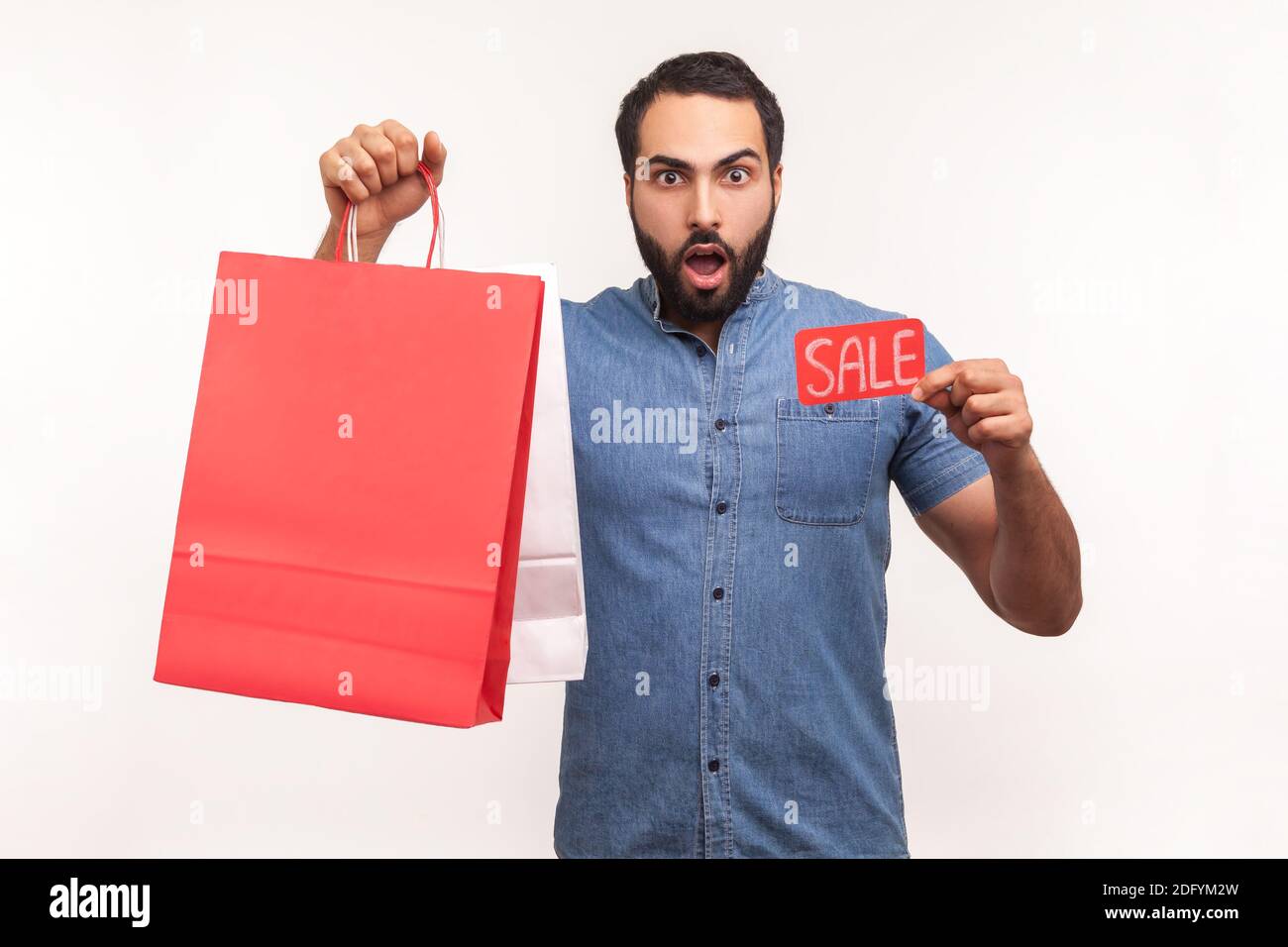 Excited surprised man holding and showing sale card and papers shopping bags, shocked with big final sale, black friday. Indoor studio shot isolated o Stock Photo